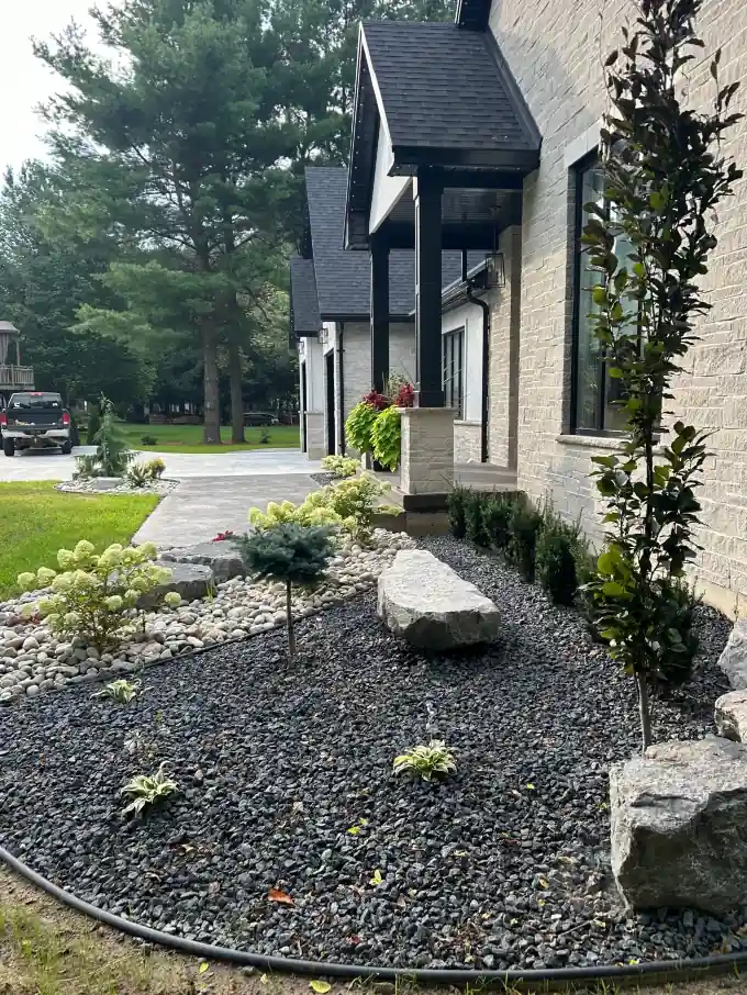 Low-maintenance rock garden with shrubs, boulders, and edging installed by Armour Designs.